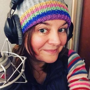 voice over Natalie Cooper in the studio wearing a winter hat and jumper, behind a Neumann TLM103 microphone