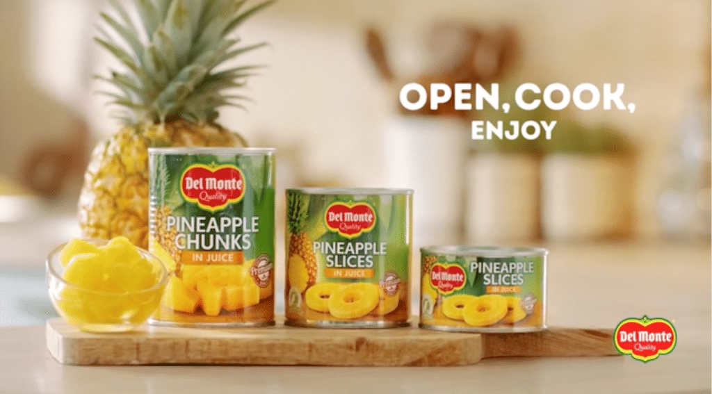 Still image from the Del Monte tv commercial showing 3 different sized tins of pineapple with the text Open, Cook, Enjoy.