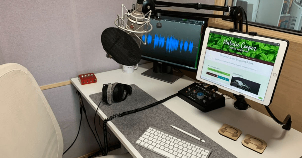 A recording studio desk, with two monitors, a wireless keyboard and microphone