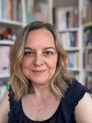 Natalie Cooper head and shoulder shot. She's looking directly into the camera, with a bookshelf behind.