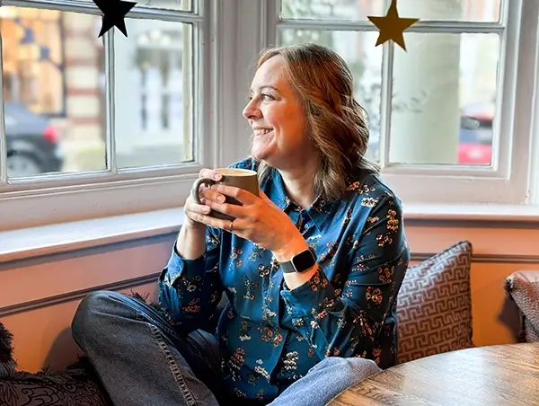 Natalie Cooper sat holding a mug, looking out of a large window.