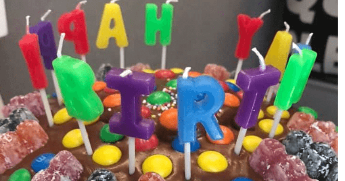 A chocolate birthday cake with brightly coloured 'Happy Birthday' candles