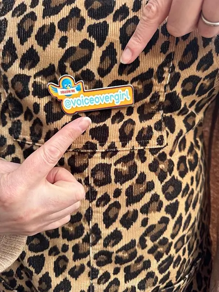 close up of Natalie Cooper pointing to a badge that says '@voiceovergirl'