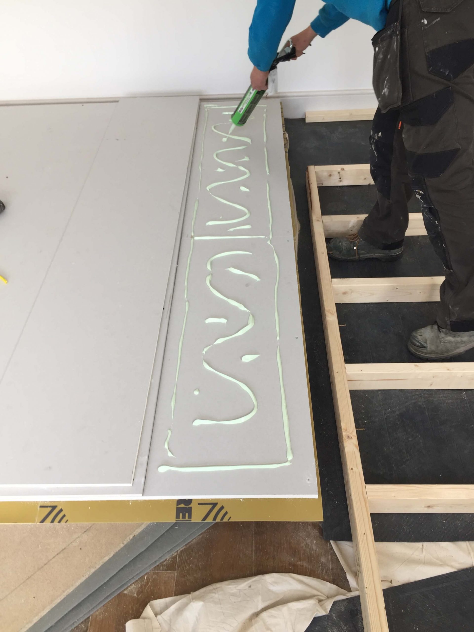 Carpenter applying Green Glue acoustic compound to soundproof plasterboard during the construction of a home voiceover recording booth.